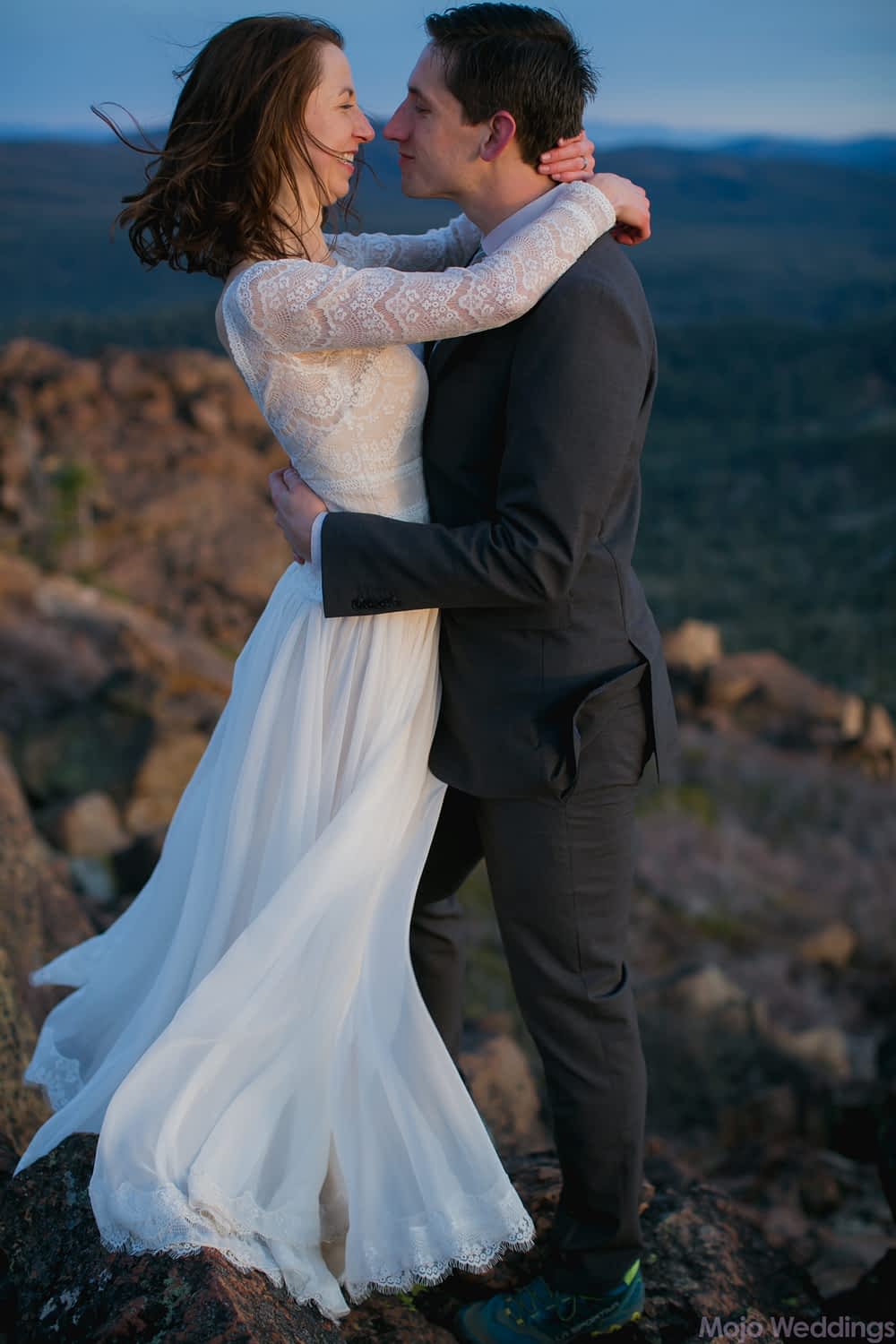A full length view of the bride and groom holding each other with her dress softly blowing in the wind.
