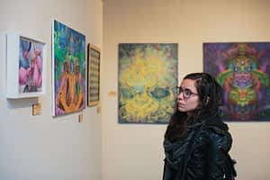 A woman dressed in black looks at a colorful, trippy painting at the grand opening of Phaneros Art Gallery.