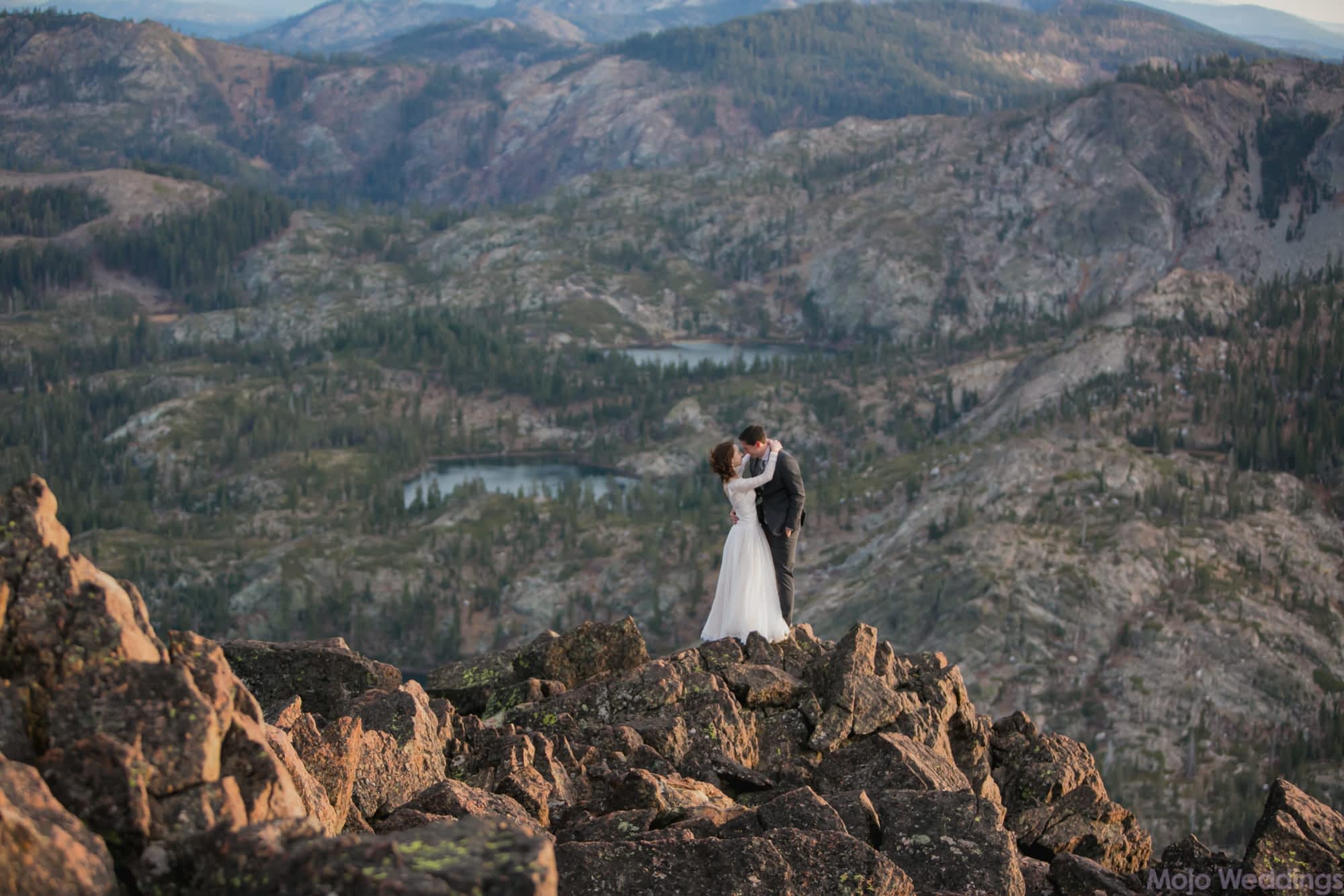 Her arms are around his shoulders as they stand against a mountain background.