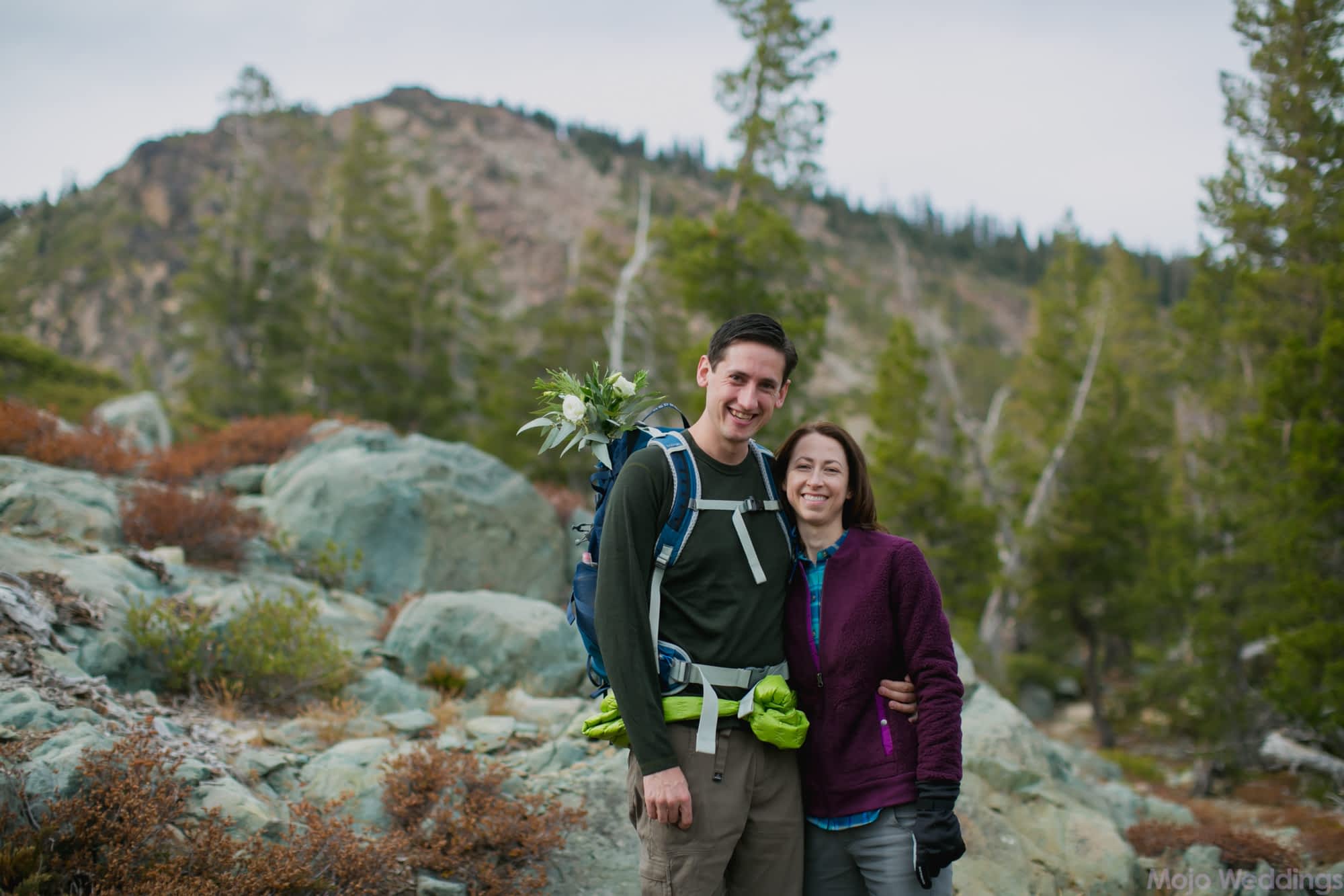 Dressed in hiking clothes, the couple smile for the camera in front of the mountain we will soon be on top of.